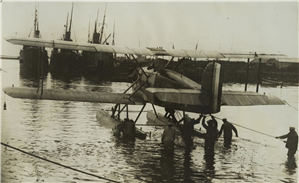 Men stand knee deep in water pulling ropes attached to a seaplane